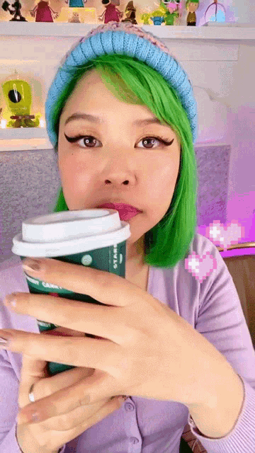 a woman with green hair is drinking from a cup that says starbucks on it