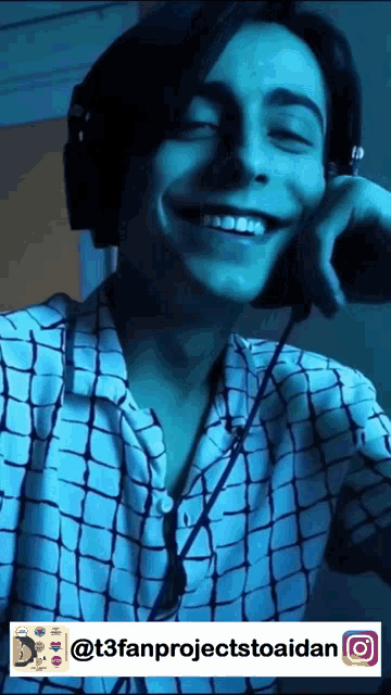 a man wearing headphones and a plaid shirt smiles for the camera