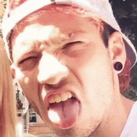 a man wearing a hat and ear plugs is sticking out his tongue .