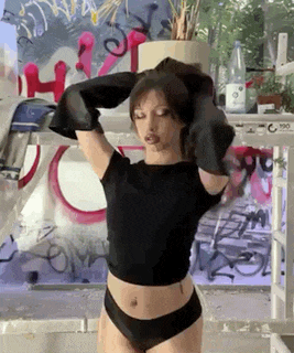 a woman in a black crop top and black panties is standing in front of a window .