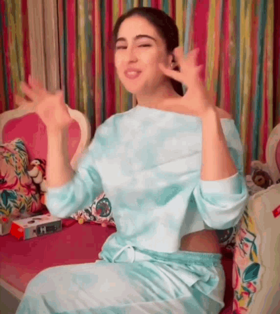 a woman in a blue tie dye top is sitting on a pink couch making a funny face .