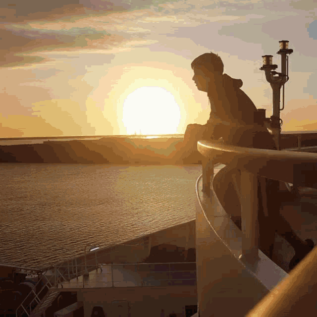 a man stands on a balcony looking at the sunset over the water