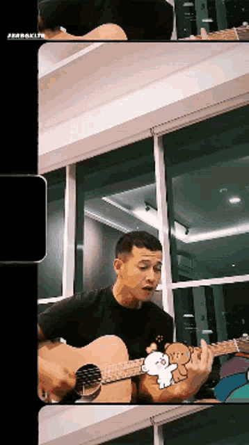 a man is playing an acoustic guitar in front of a window with a teddy bear on it