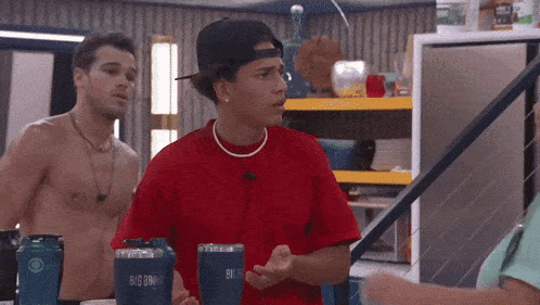 a man in a red shirt is standing next to a man in a black hat holding a big bro tumbler