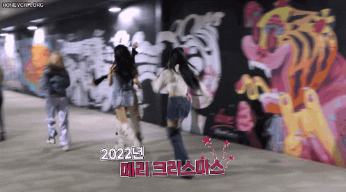 a group of girls are dancing in front of a wall with graffiti on it that says 2022