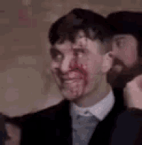 a man in a suit with blood on his face is smiling .