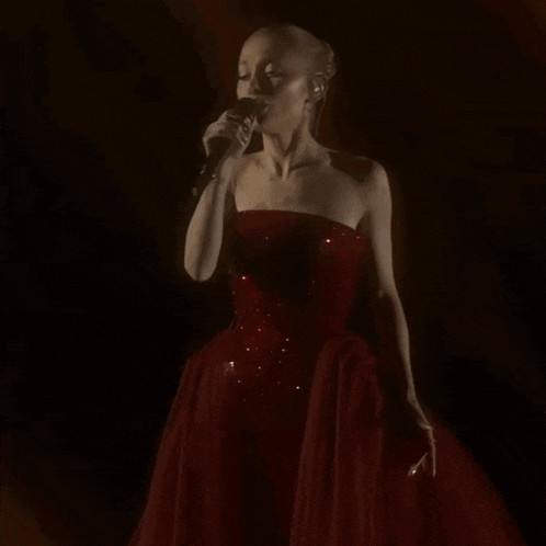 a woman singing into a microphone in a red dress