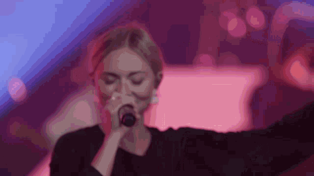 a woman is singing into a microphone in front of a pink background
