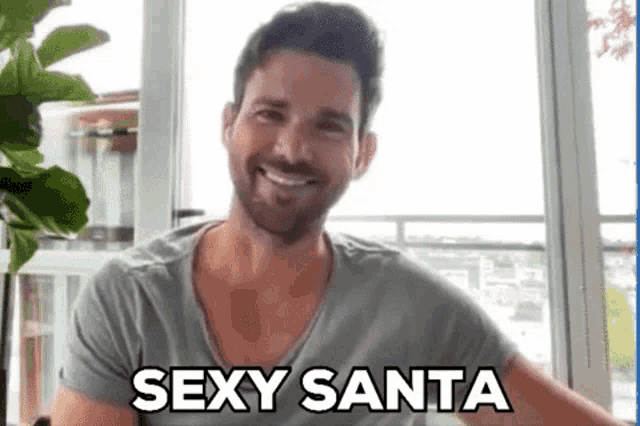 a man with a beard is sitting in front of a window and smiling .