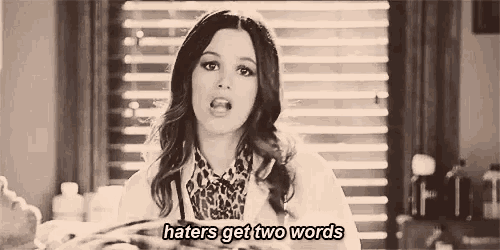 a woman is standing in front of a window holding a piece of paper and says `` haters get two words '' .