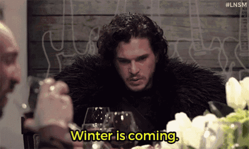 a man in a fur coat is sitting at a table with a glass of wine .