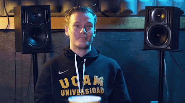a man wearing a hoodie that says ucam on it is holding a cup of popcorn