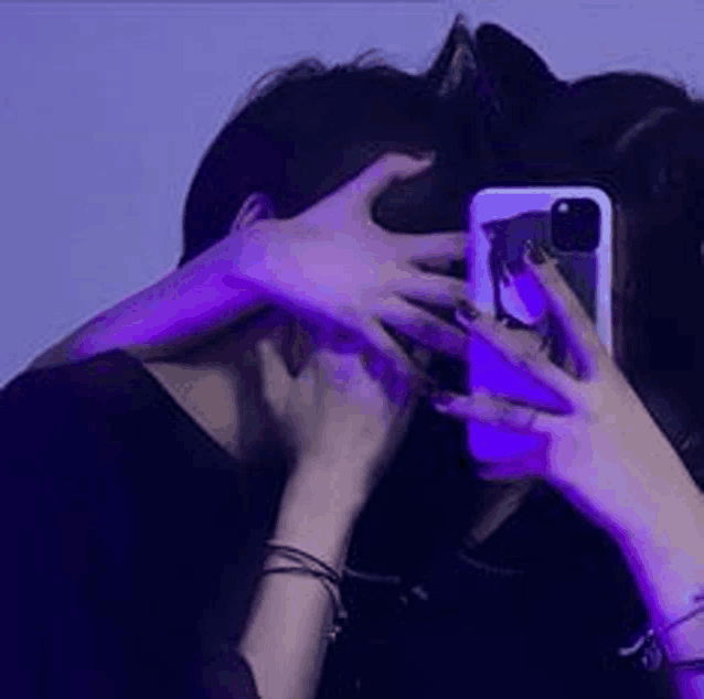 a woman is covering a man 's face with her hands while taking a selfie with her phone .