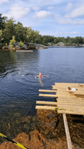 a man is swimming in a lake next to a wooden platform