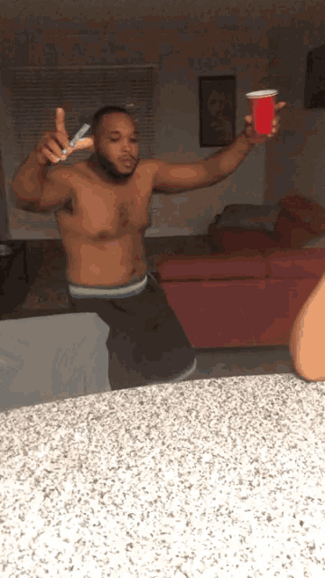 a shirtless man holds a red cup in his hand