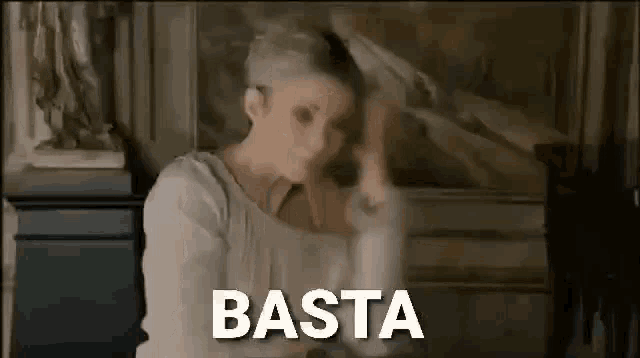 a woman is standing in front of a painting with the word basta written on the bottom .
