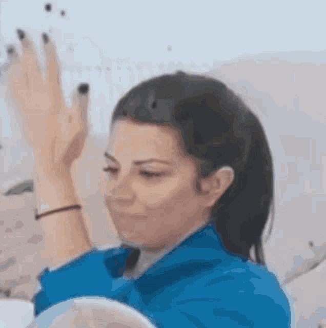 a woman in a blue shirt is sitting on a couch with her hands up .