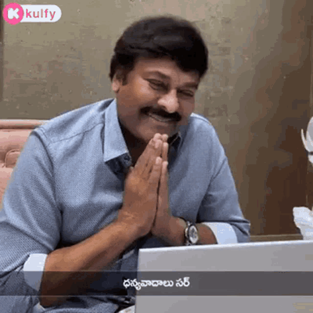 a man is sitting in front of a laptop computer with his hands folded in prayer .