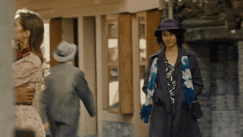 a woman wearing a purple hat and a blue scarf walks down the street