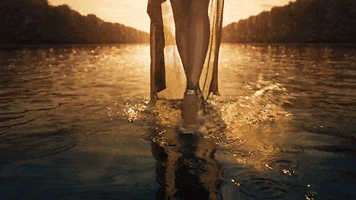 a woman is walking through the water at sunset .