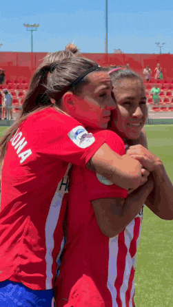 two female soccer players are hugging each other on the field .