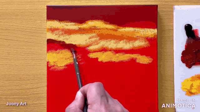 a person is painting a red sky with yellow clouds with a brush .