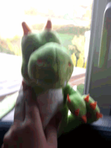 a person is holding a green stuffed animal with red spikes on its feet