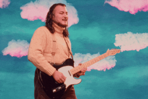 a man in a tan sweater is playing a guitar with pink clouds in the background