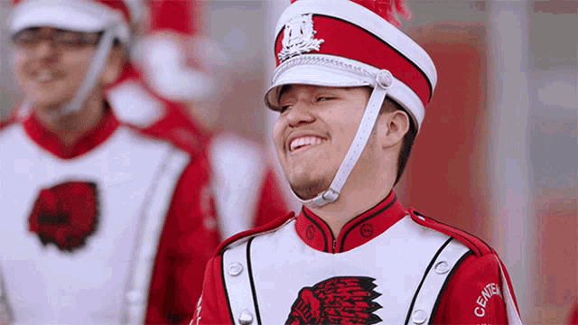 a man in a marching band uniform is smiling and wearing a red hat