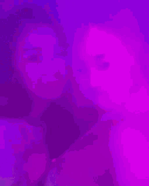two girls are standing next to each other in a dark room with purple lights behind them .