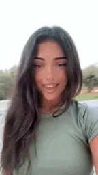 a woman with long dark hair is smiling for the camera while wearing a green shirt .