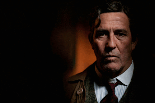 a man in a suit and tie looks at the camera with a serious look on his face