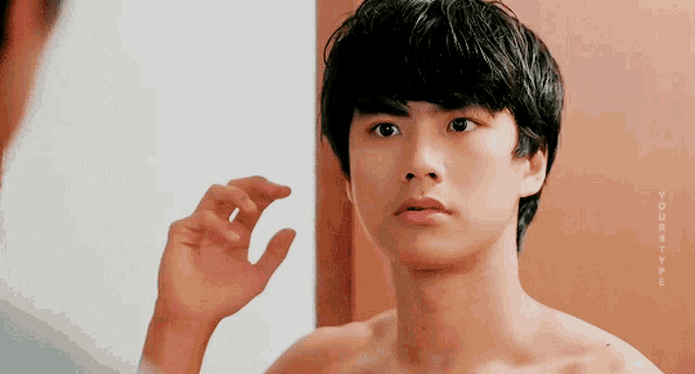 a shirtless young man looks at himself in a mirror