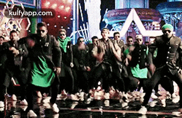 a group of men are dancing on a stage in front of a large screen .