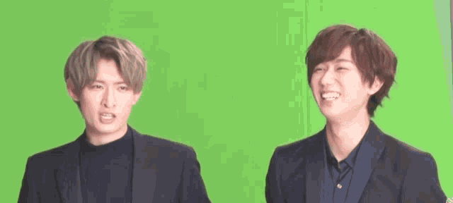 two men in suits are standing next to each other on a green screen and smiling .