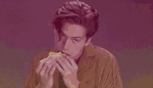 a man in a fringed shirt is eating a sandwich with his eyes closed .