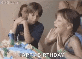 a girl is blowing out a candle on a birthday cake while a boy looks on .