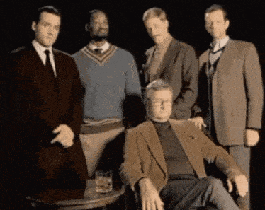 a group of men are posing for a picture while one man is sitting in a chair .