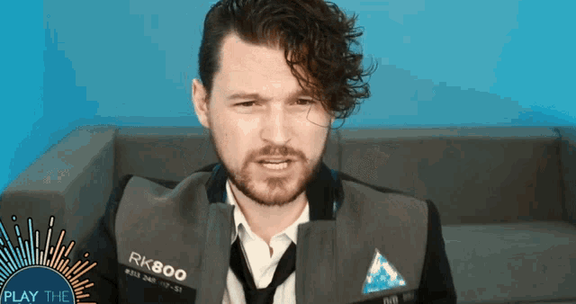 a man wearing a jacket that says rk800 is sitting on a couch
