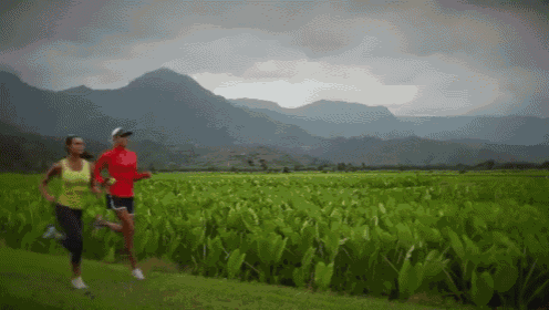 a couple of women running in a field with mountains in the background
