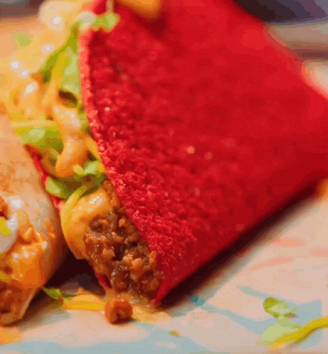 a close up of a red taco with meat and cheese on a plate