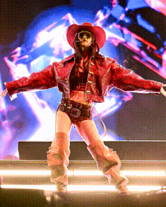 a woman in a cowboy hat and sunglasses is dancing on a stage