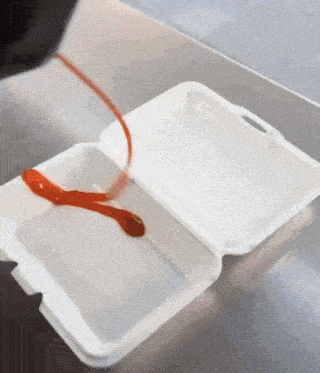 ketchup is being poured into a styrofoam container on a counter