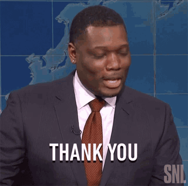 a man in a suit and tie is giving a thank you gesture