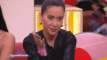 a woman is sitting in front of a sign that says #grandefratello on it