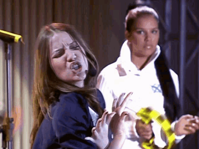 a woman making a funny face while another woman holds a yellow tape