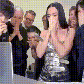 a woman in a silver dress is covering her face while a group of people look at a laptop .