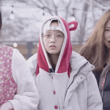 a girl wearing a bear hooded jacket and glasses stands with two other girls