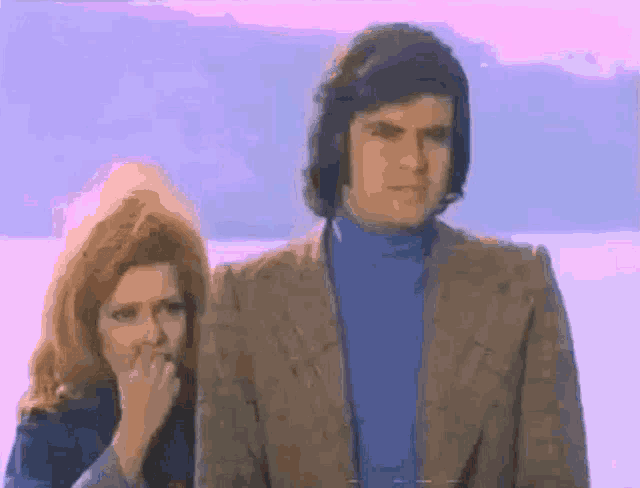 a man and woman are standing next to each other and the woman is covering her mouth