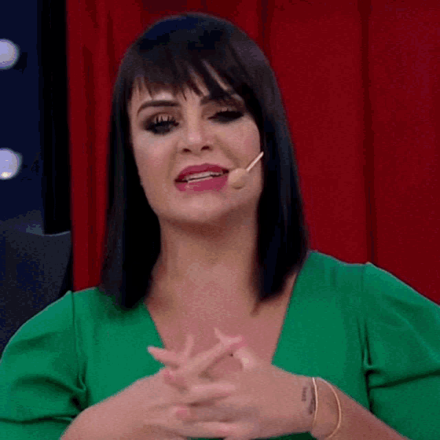 a woman wearing a green shirt and a gold bracelet is talking into a microphone